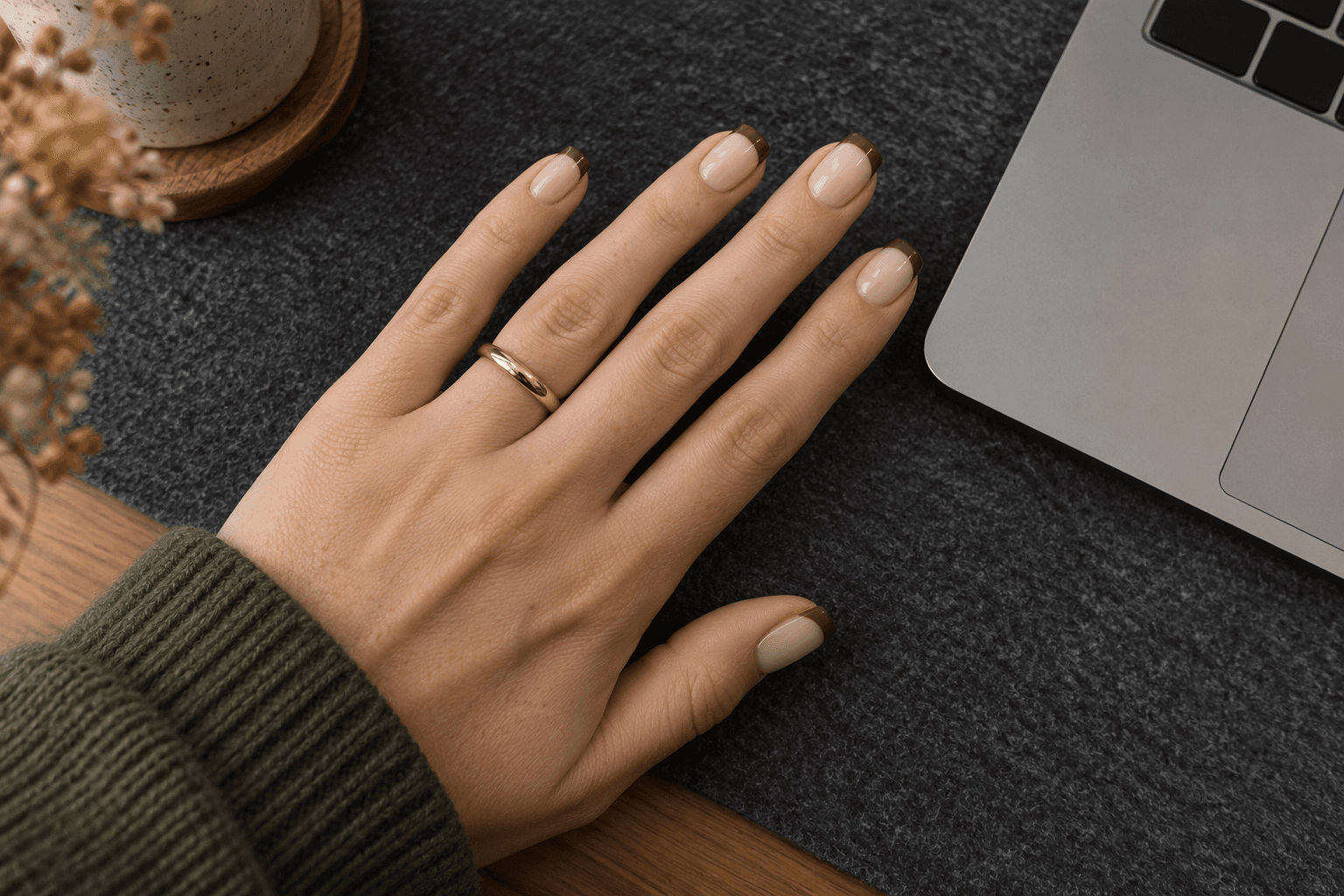 Short pink-beige nails with narrow curved brown French tips on a felt desk mat.