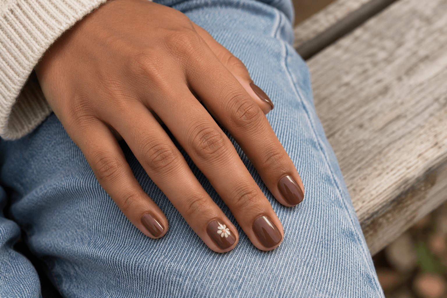 Short glossy mocha nails with a single cream flower accent, resting on blue denim.