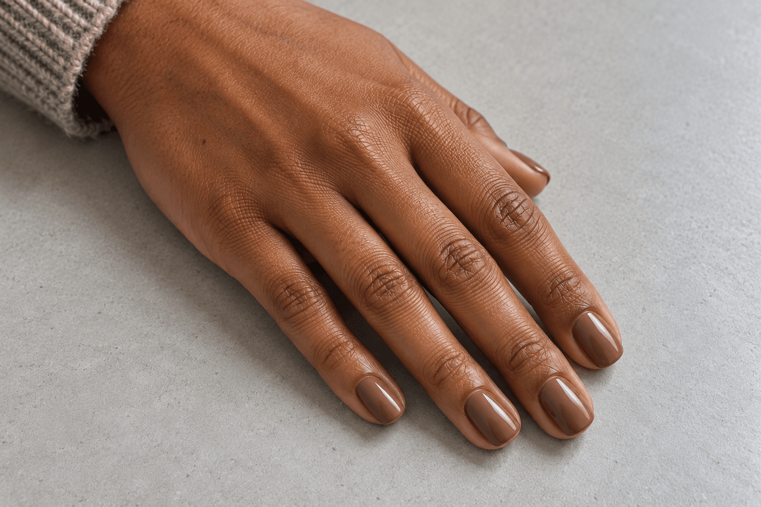 Four visible short squoval nails in a soft beige-brown mocha color on a neutral gray surface.