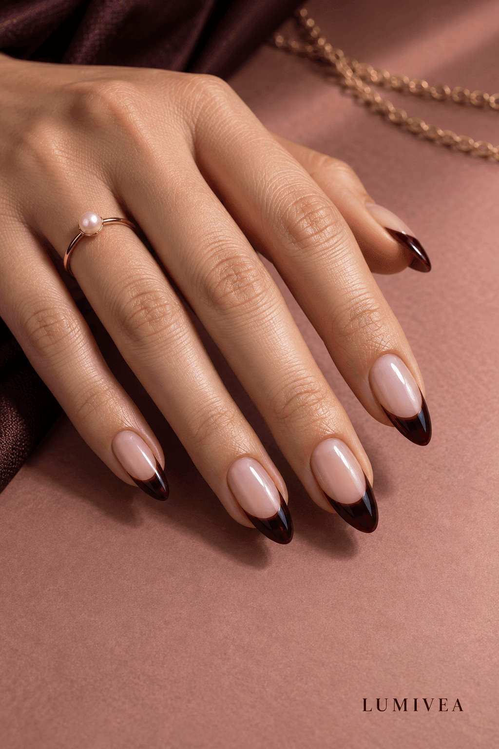 Black-cherry French-tip almond nails on a dusty-rose background with a small Lumivea logo