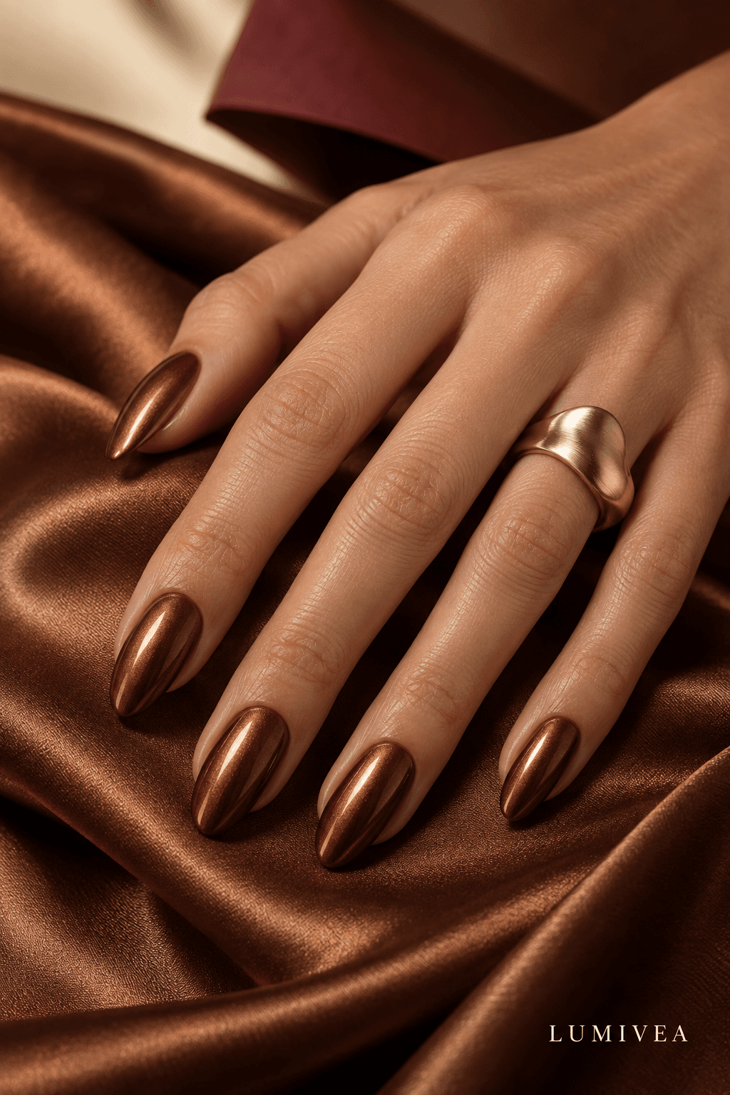 Cinnamon-brown almond nails with a fine copper chrome finish and a small Lumivea logo