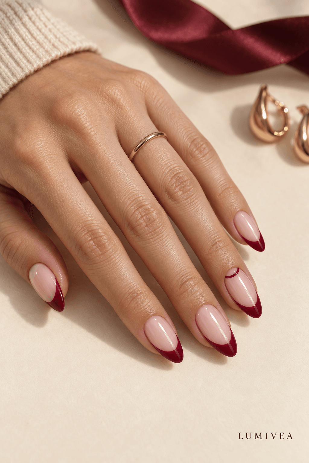 Cranberry-red French-tip almond nails on a warm cream background with a small Lumivea logo
