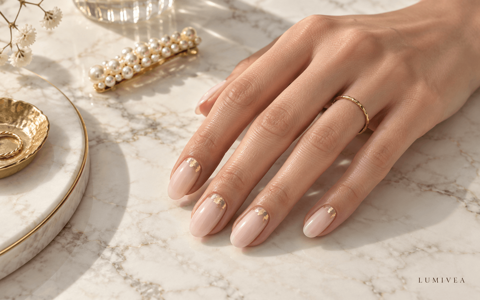 Sheer milky nude nails with delicate gold foil accents on ivory marble and a Lumivea watermark