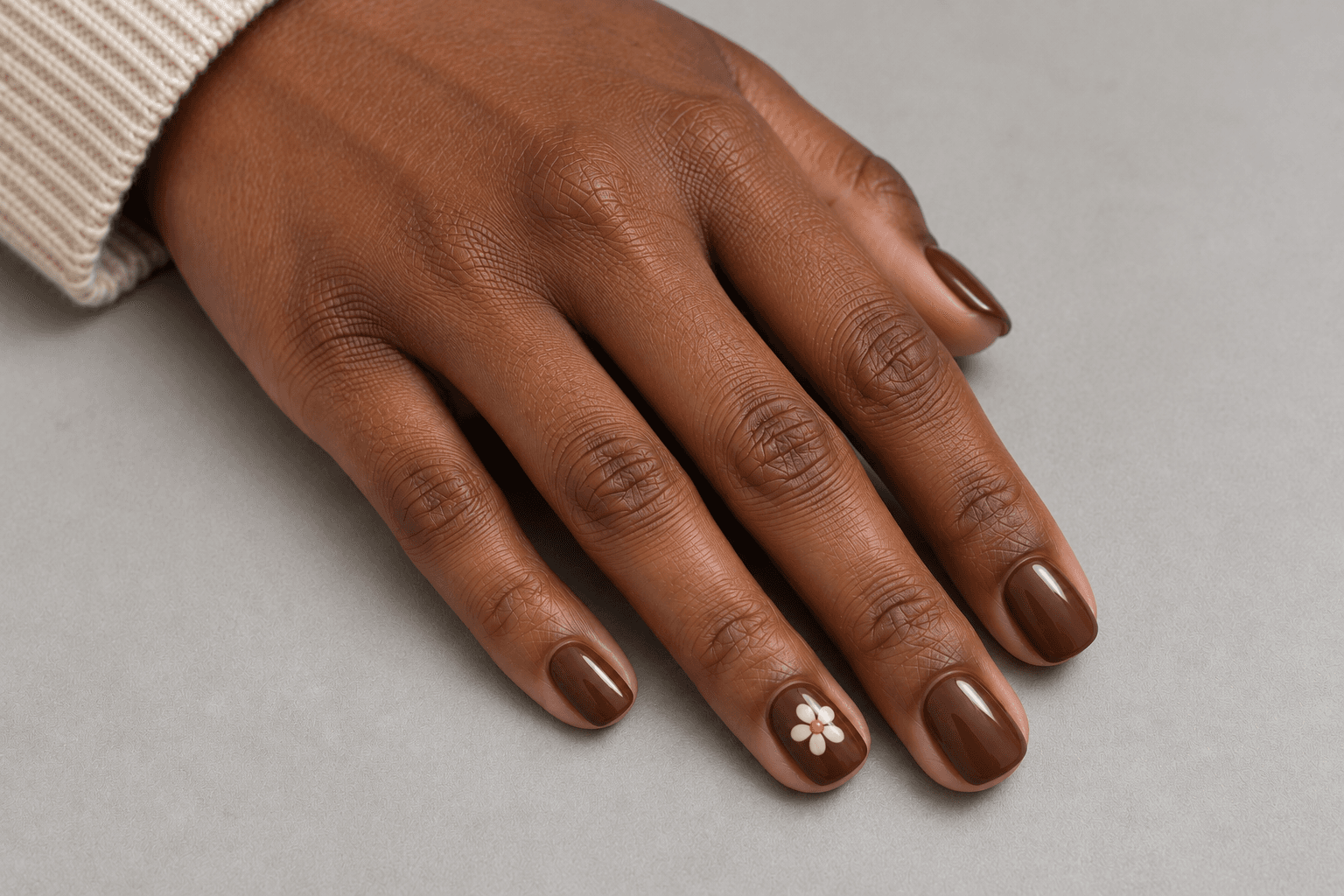 Short chocolate-brown nails with one simple cream daisy on an accent nail.