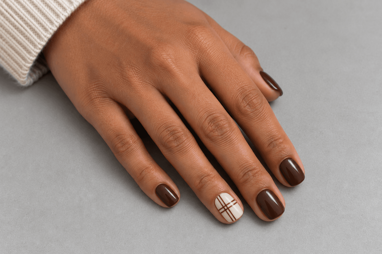 Short brown nails beside one cream accent with a few crossing brown lines.