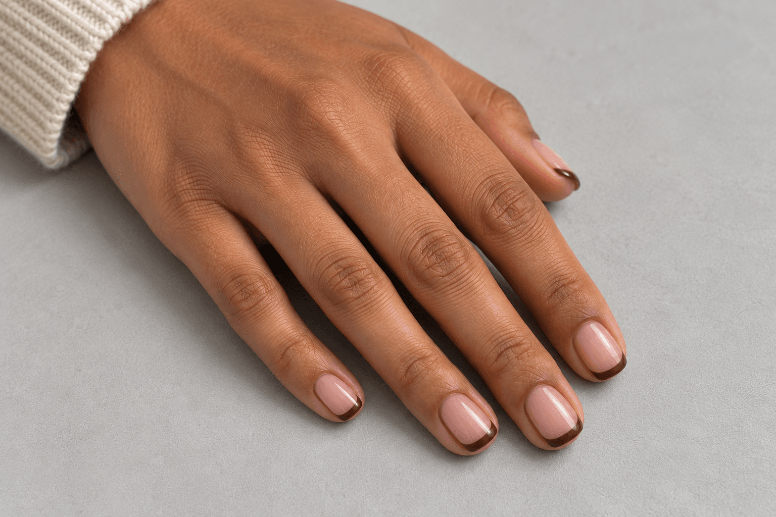 Short pale pink-beige nails with narrow curved brown French tips.