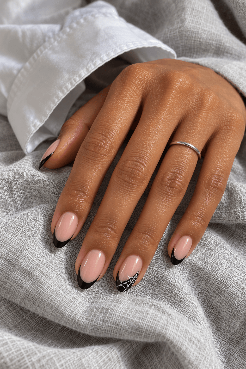 Almond nails with pale bases, slim black French tips, and a small white web inside one dark tip.